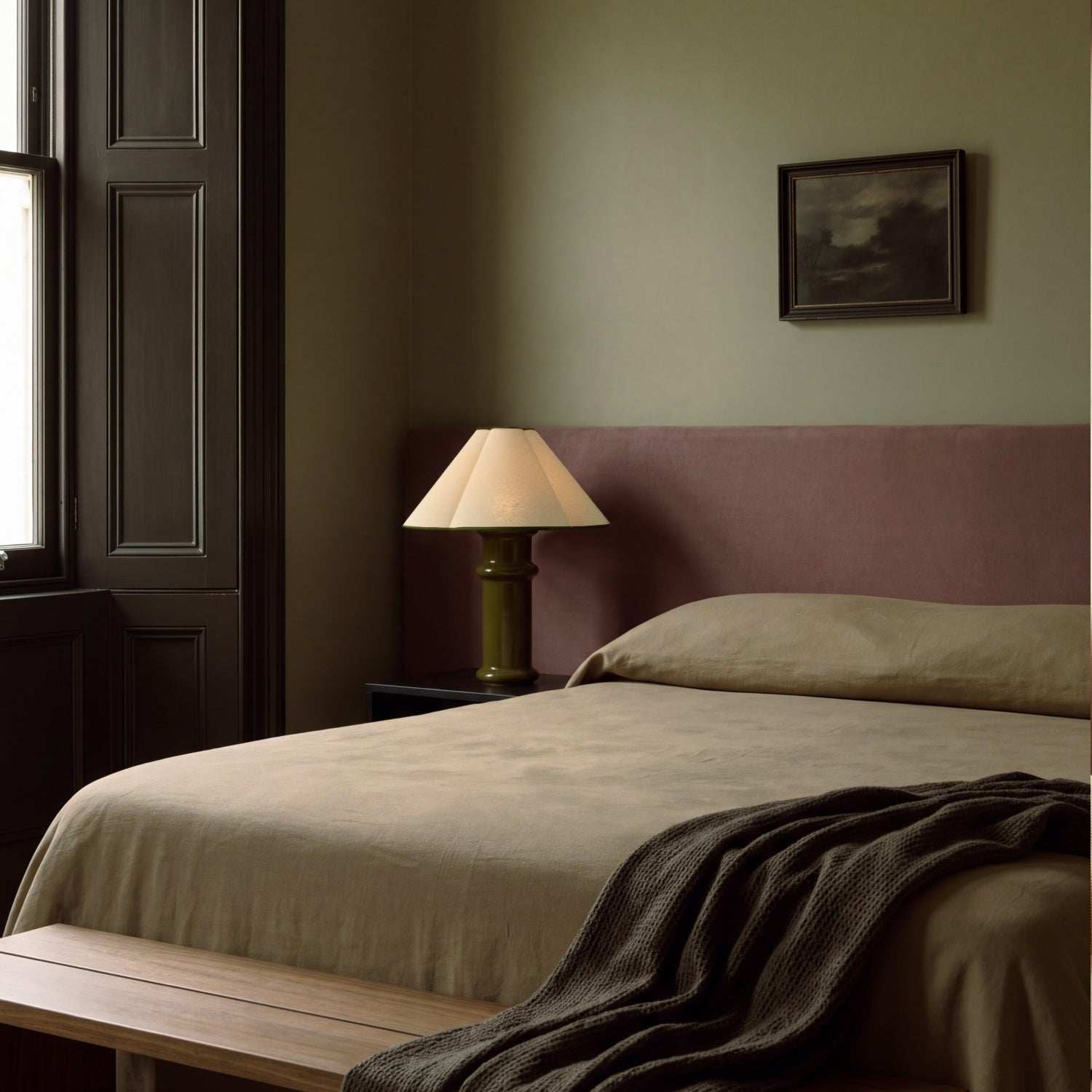 Lit Heath Table Lamp on a bedside table in a sage green bedroom with a plum upholstered headboard