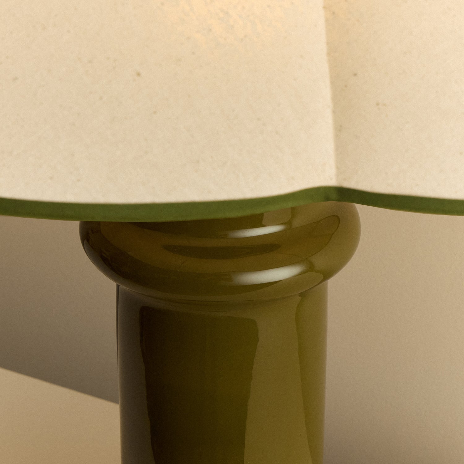 Close-up of the Heath Table Lamp's glossy olive green ceramic base below the green-edged scalloped shade