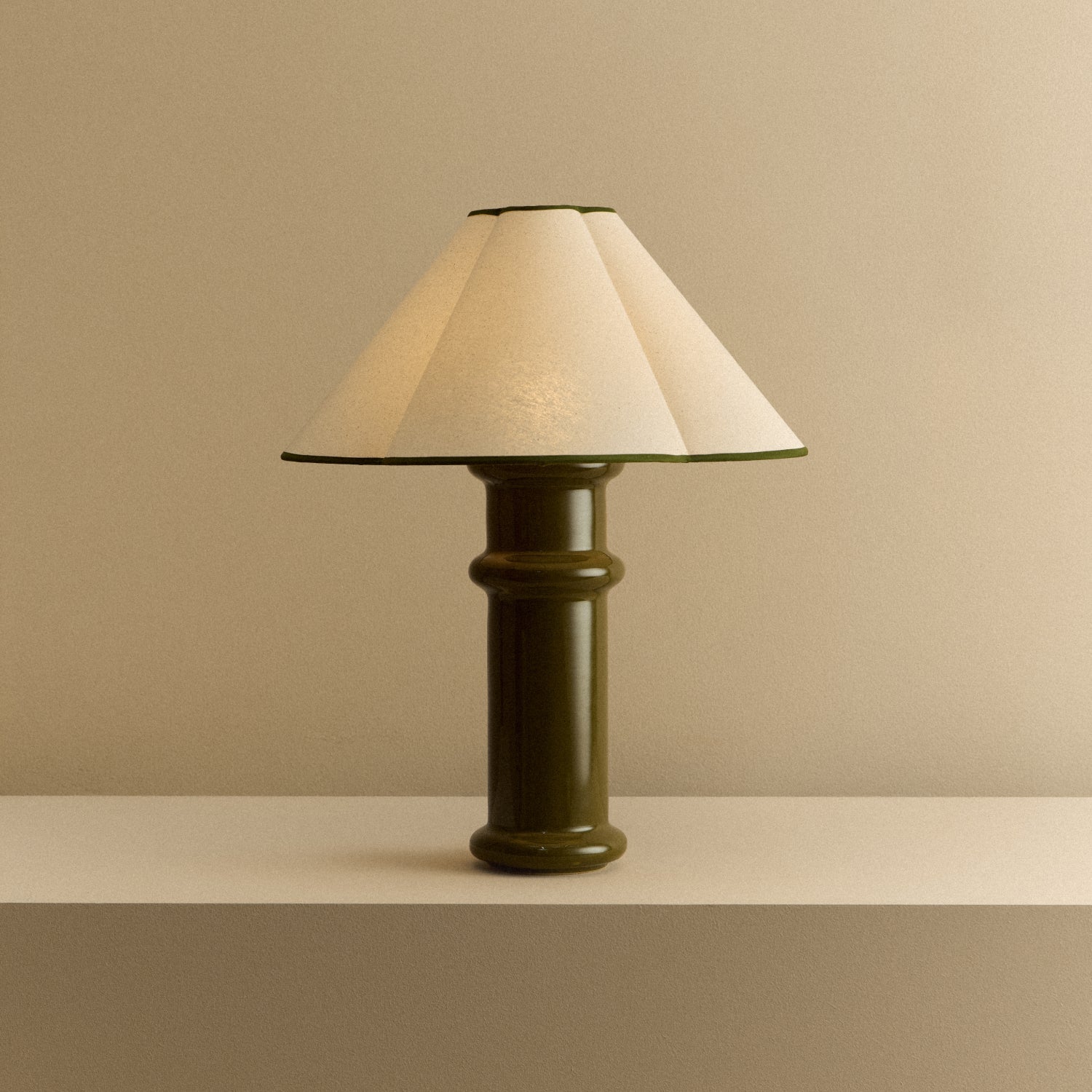 Heath Table Lamp in Olive Green switched on: a glossy olive green turned ceramic base with a scalloped cotton shade edged in green