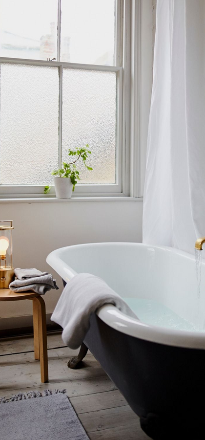 The Muse Portable Lamp in Solid Brass next to a bathtub in a bathroom setting. The Muse is the perfect self care companion, portable to any space and providing a perfect glow to set the mood anywhere.